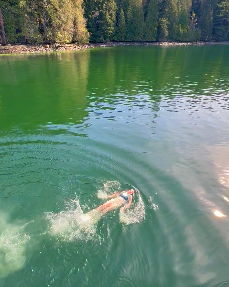 Person swimming in clear ocean water next to the Hot Voyage sauna boat.