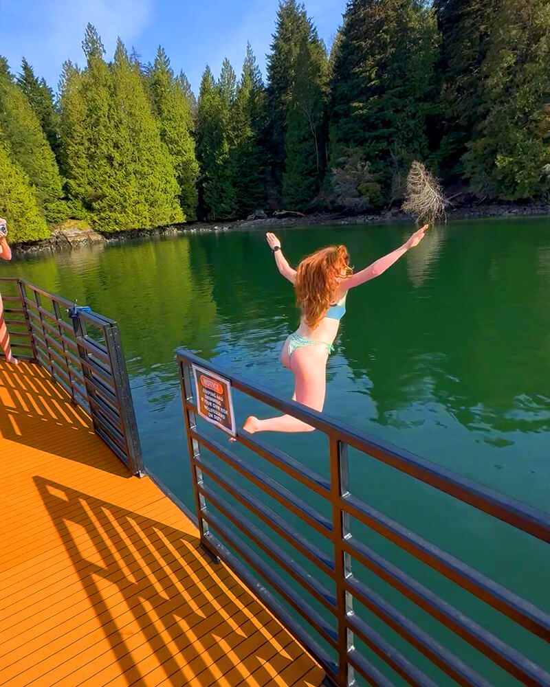 Woman mid-air jumping off the roof of the Hot Voyage sauna boat into the water.