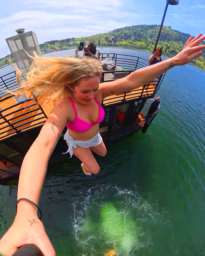 Woman taking an action selfie mid-air jumping off the Hot Voyage sauna boat.