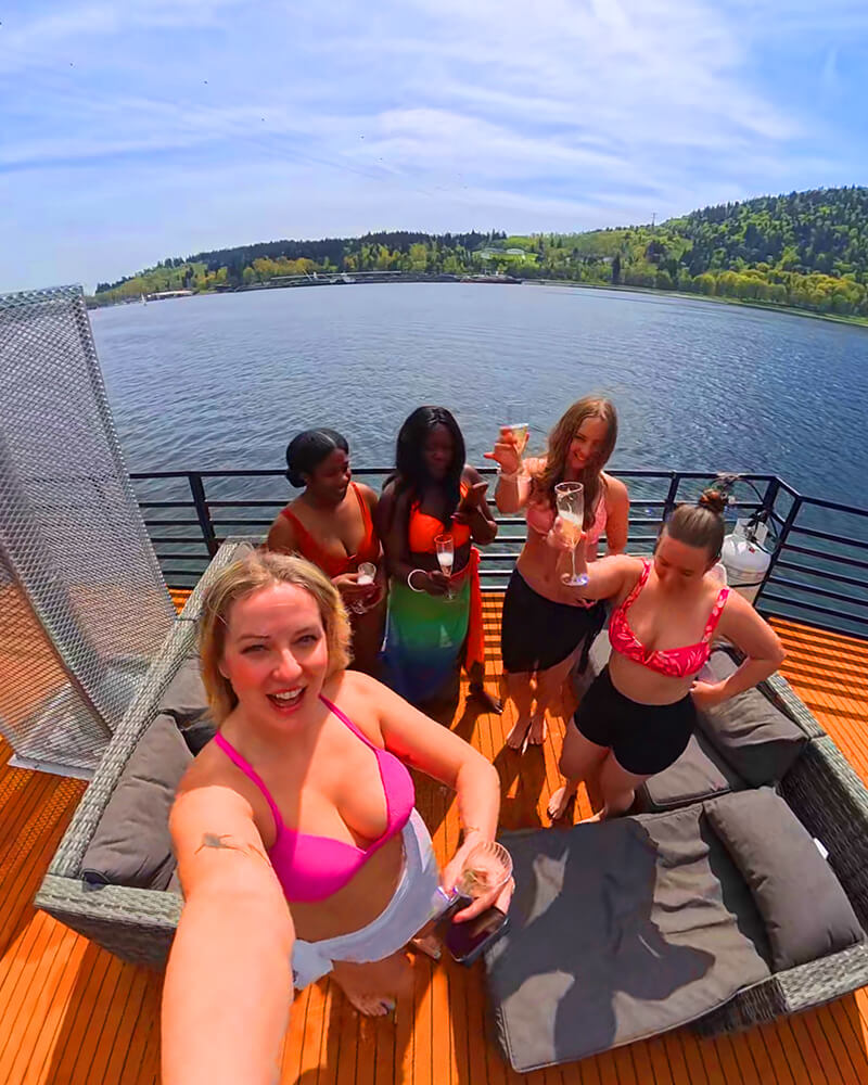 Group of friends relaxing and smiling on the rooftop deck of the Hot Voyage sauna boat.