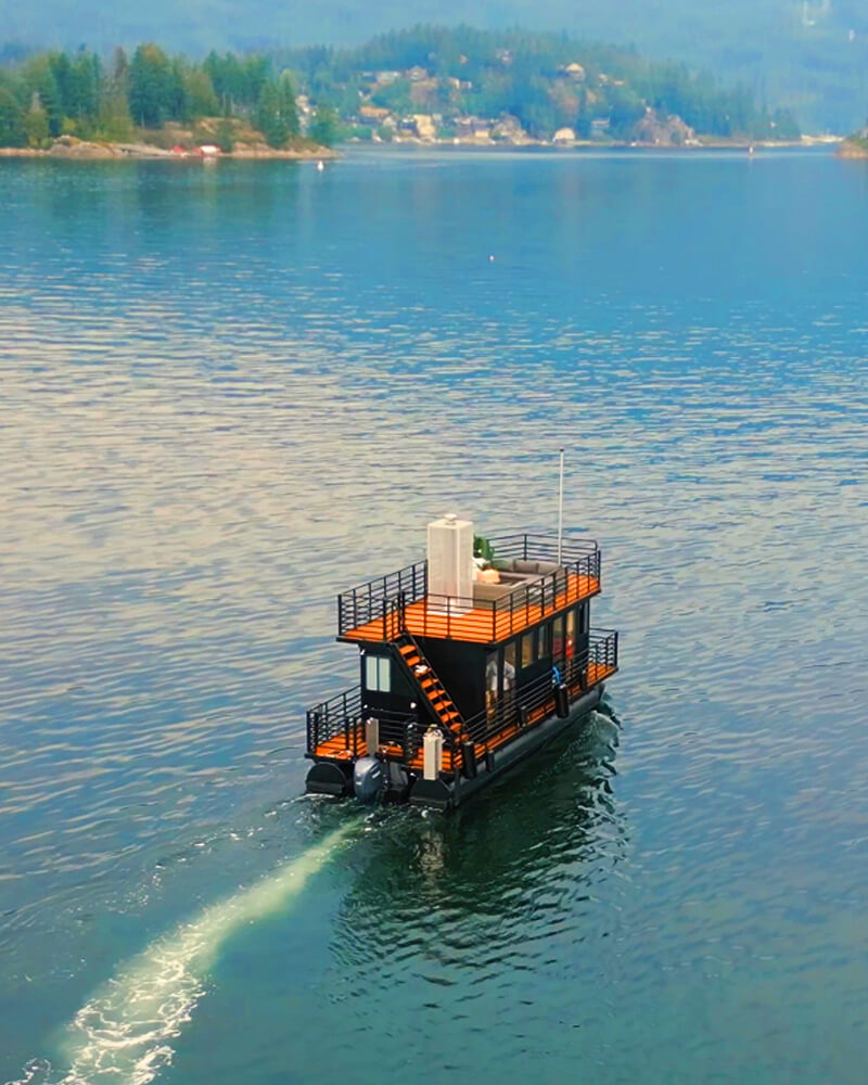 Aerial view of a Hot Voyage sauna boat cruising through a forested fjord.
